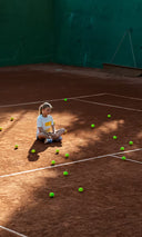 Girl sitting on a tennis court with scattered tennis balls