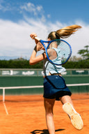 Girl in action on a clay court with a blue sky while playing in Roggio outfit.