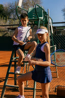 Two children on a tennis court with tennis rackets posing for Roggio