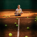 Girl sitting on a tennis court surrounded by tennis balls uring Roggio shooting