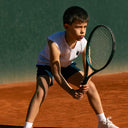 Young boy playing tennis on a clay court wearing Roggio top 